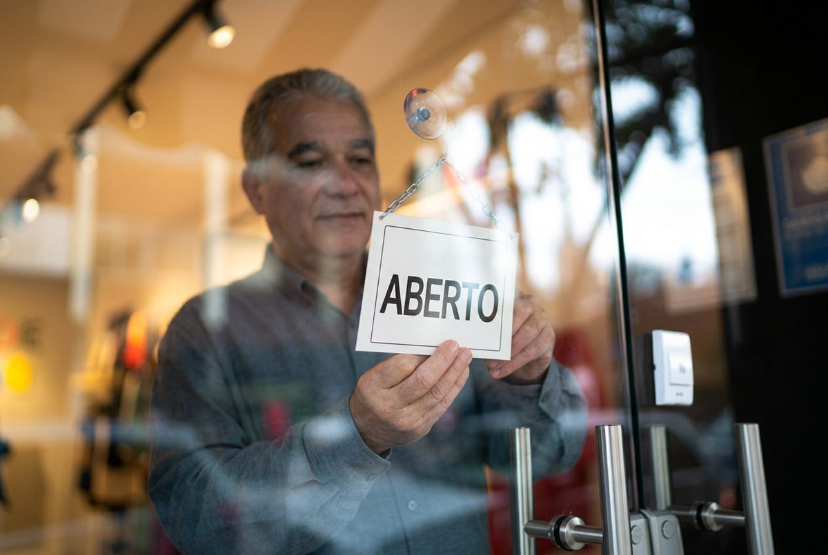 Comerciante a pendurar uma placa de aberto na porta de vidro de uma loja de rua